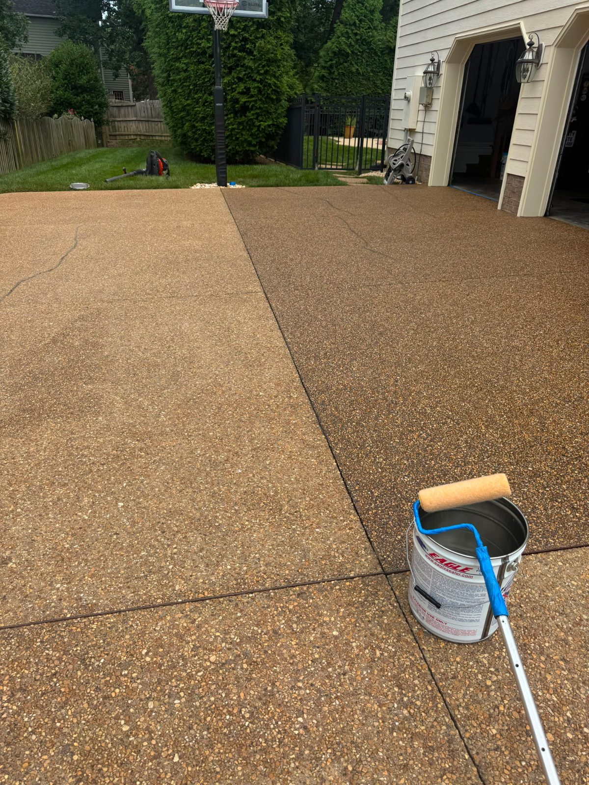 Driveway coating in progress with a roller and paint can