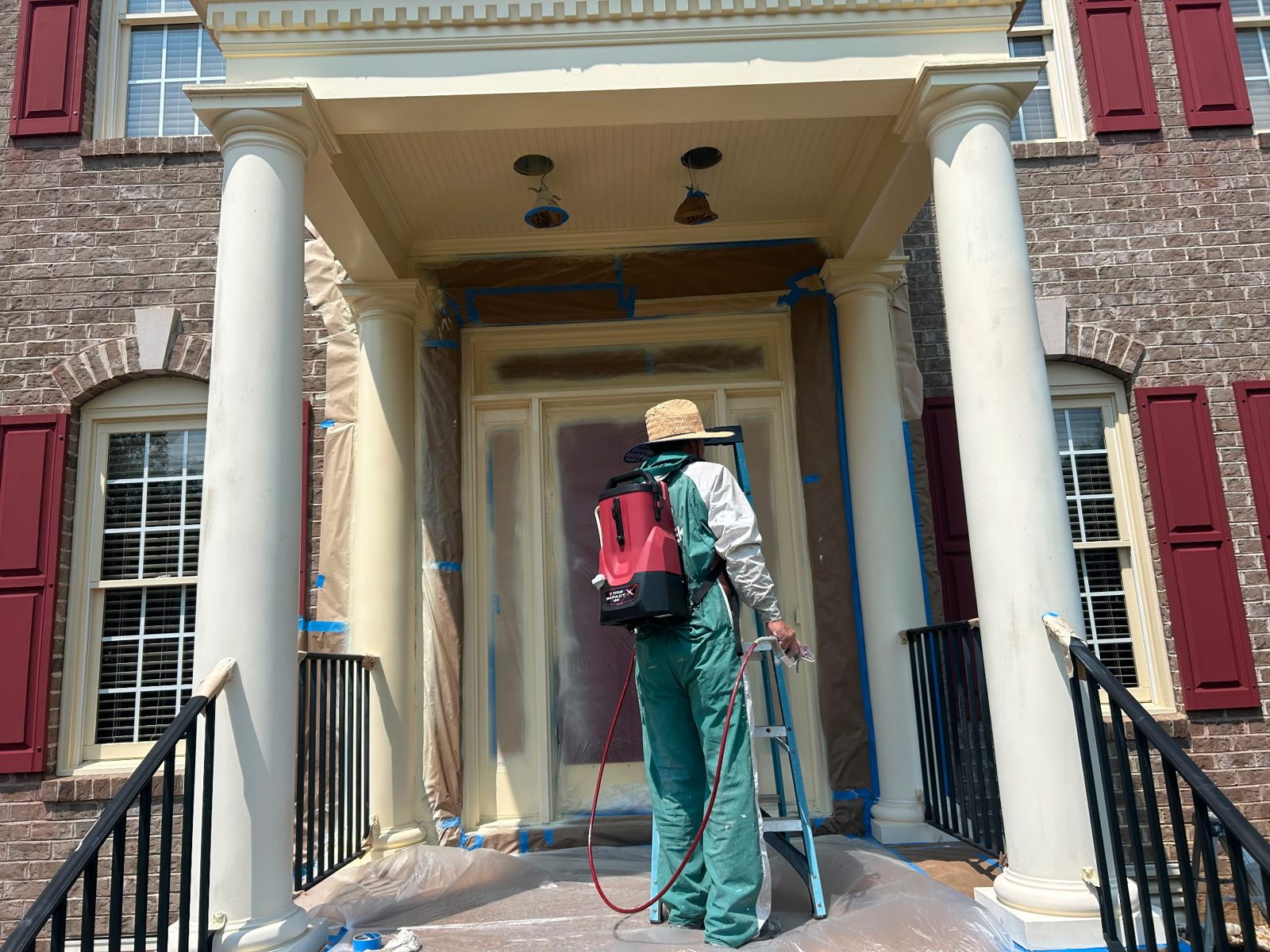 A JAM painter spraying the front entry of a brick colonial home